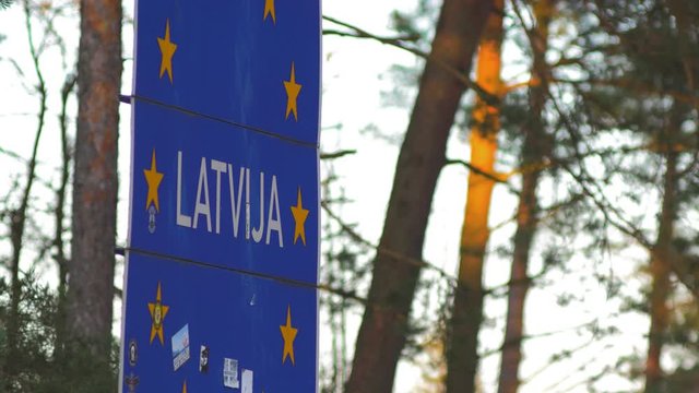 European Union border sign at the Latvia - Lithuania border, pine forest in background, medium shot at golden hour