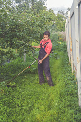 female worker mows the grass with a trimmer in the garden