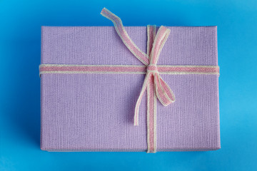 Gift pink-violet box with a tied ribbon and threads, on a blue cyan background top view