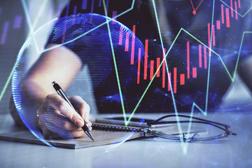 Multi exposure of woman's hands making notes with forex graph hologram. Concept of technical analysis.