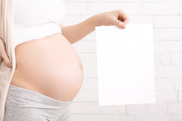 Pregnant woman holding blank white card near naked belly