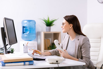 Young contemporary office manager or head of business company sitting by desk