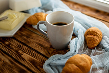on a wooden table with blue gauze is a gray cup with coffee nearby in blur croissants