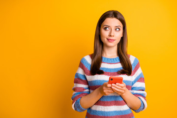 Portrait of her she nice attractive curious pensive bewildered brown-haired girl holding in hands cell thinking creating plan isolated over bright vivid shine vibrant yellow color background