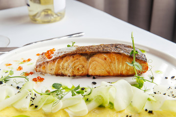 Fried salmon with mashed potatoes and red caviar on a white plate, closeup, side view, horizontal
