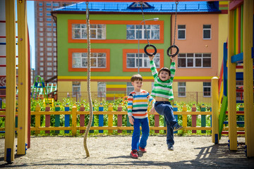 Two brothers sibling boy in casual clothes on playground climbing rope and athletic rings. Kids has a lot of fun. Healthy leisure time with children. Family competition friendship concept