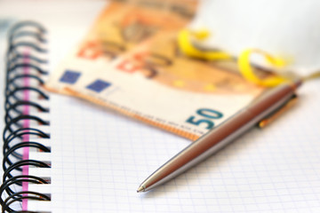 Luxury Pen, Protective mask and 50 Euro bank notes on a white paper copybook background.