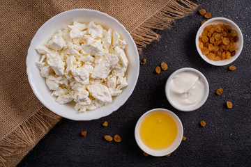 Cottage cheese in a white plate, separately honey, raisins on burlap, a dark background.  Top view.