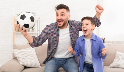 Emotional dad and son with football ball watching sport on tve