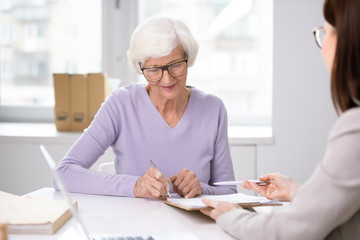 Senior client putting her signature in insurance agreement after consulting
