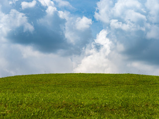 Green grass on small hill and blue sky with clouds