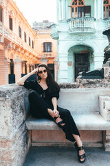 Girl in black overalls sits on a bench among old Spanish-style colonial houses