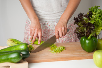 Woman chopping celery vegetable, preparing food in her kitchen, she is cutting fresh celery on a cutting board with a knife. Wooden board.