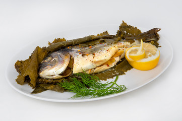 Baked fish in grape leaves with spices and stuffed with lemon. Garnished with lemon and a sprig of dill