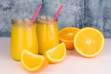  Two servings of orange juice in glass jars and fresh oranges on the table. Close-up.