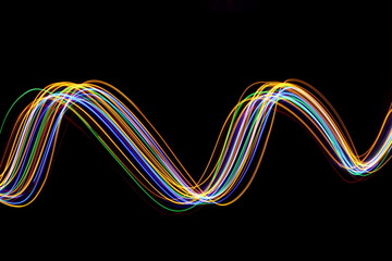 Multi color light painting photography, gold, red, green and blue waves of vibrant color against a black background