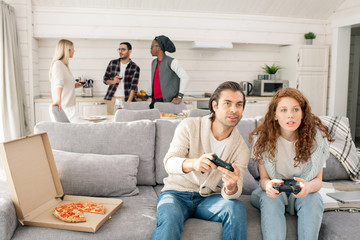 Young couple sitting on couch in front of tv set and playing video games