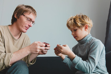 father and son looking at mobile phones at home, family playing games