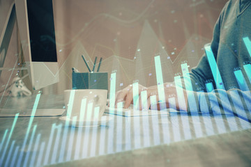 Multi exposure of graph with man typing on computer in office on background. Concept of hard work.