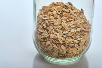 oatmeal lies in a glass jar, which stands on a white reflective surface.