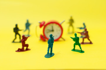 Toy soldiers surrounding a fallen alarm clock. Killing time, wasting time, stop time, time management, deadline, overtime concept.