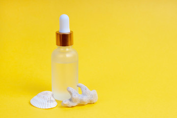 Face care in a glass dropper bottle with sea shell and coral on a yellow background. Skin care concept. Horizontal photography