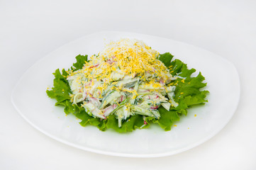 Spring salad of cucumber, radish, grated egg on lettuce. Salad is presented on a square plate on a white background.