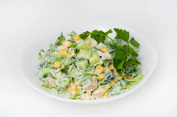 Vegetable salad of cucumbers, sweet pickled corn, greens and mayonnaise in a white deep plate on a white background