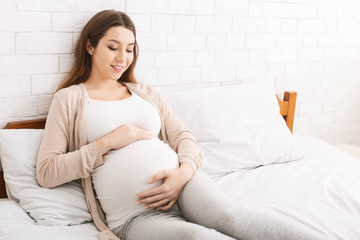Young expectant woman touching her belly in bed