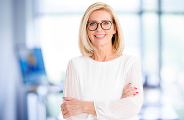 Fototapeta premium Portrait shot of attractive senior businesswoman standing in the office with arms crossed