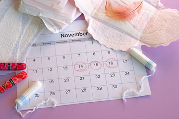 Menstrual pads and tampons on menstruation period calendar with on lilac background.