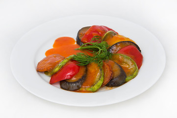 Fried sliced eggplant, zucchini, tomato in tomato sauce with a sprig of dill on a white round plate on a white plate