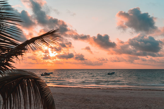 Palm leaves and fishing boats at sunrise on the sandy beach of the Caribbean