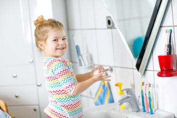 Cute little toddler girl washing hands with soap and water in bathroom. Adorable child learning cleaning body parts. Hygiene routine action during viral desease. kid at home or nursery.