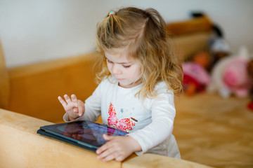 Cute little toddler girl playing with tablet pc at home. Healthy baby touching pad with fingers, looking cartoons and having fun with educational games on computer. on quarantine against coronavirus