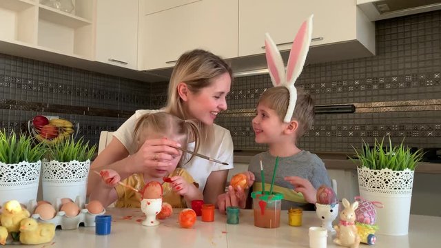 Happy easter! A mother and her daughter and son painting Easter eggs. Happy family preparing for Easter. Cute little child boy wearing bunny ears on Easter day.
