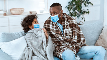 Fototapeta premium Coronavirus health alert. Little girl with her African American grandfather wearing protective masks at home