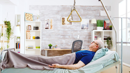 Old retired and disabled man lying in a hospital bed in a nursing home