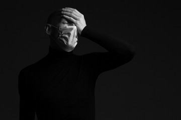 Coronavirus, Bio Protection Concept. Close up portrait of handsome bald man wearing medical mask, black turtleneck, hiding face with hand. Copy-space. Monochrome studio shot