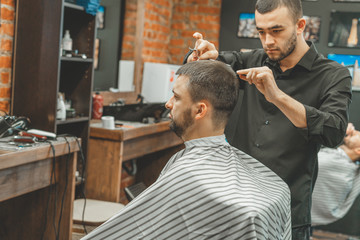 Fototapeta premium Haircut at the hairdresser. Barber cuts the hair on the client's head. The process of creating hairstyles for men. A man in a barbershop. The near plan. Equipment stylist. Selective focus