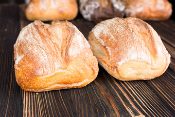 A variety fresh homemade loaves of ciabatta on a dark wooden background.