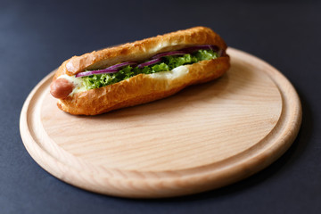Close up of hot dog lying on the wooden plate. Fast food. Isolated over black background.