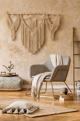 Stylish oriental living room with design armchair, beautiful macrame, wooden ladder, pouf, decoration, carpet, pillow, books and elegant personal accessories in wabi sabi concept. 