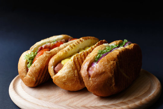 Three hot dogs lying on the wooden plate.