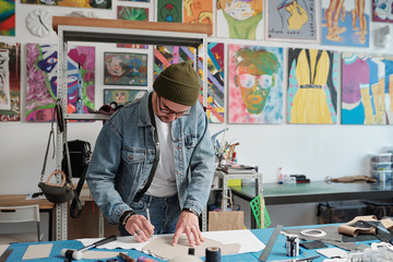 Contemporary leatherworker bending over table while outlining paper pattern