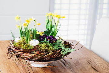 Easter table centerpiece decoration with daffodils and easter eggs arranged in a rustic wreath made of tree twigs