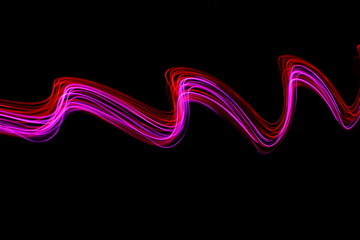 Pink and red light painting photography, waves of vibrant color against a black background.  Long exposure photo of vibrant fairy lights in abstract swirl.