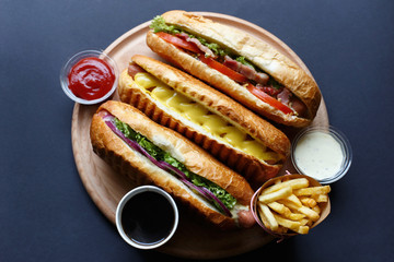 Three hot dogs, sause, ketchup, coffee, French fries lying on the wooden plate.  Mock up.