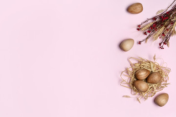 Wooden Easter eggs in a straw nest, decorated by a bunch a dried flowers, on a pink background.