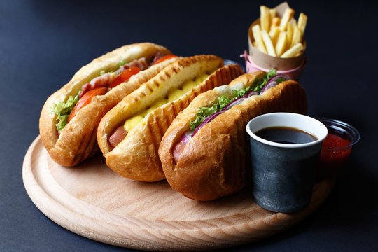 Three hot dogs, ketchup, coffee, French fries lying on the wooden plate.  Mock up.